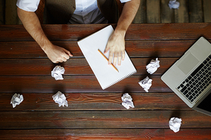 Wooden table with crumpled papers, laptop and notepad with pencil during work of creative designer