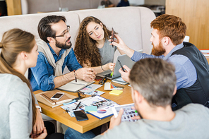 Young designer showing his colleagues something curious in smartphone