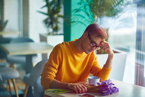 Portrait of sad young man sitting alone in cafe with bouquet of flowers