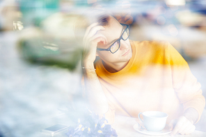 Portrait of romantic young man daydreaming while waiting for date in cafe with bouquet of flowers and cup of coffee