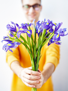 Portrait of smiling young man presenting bouquet of flowers to camera, focus on beautiful irises