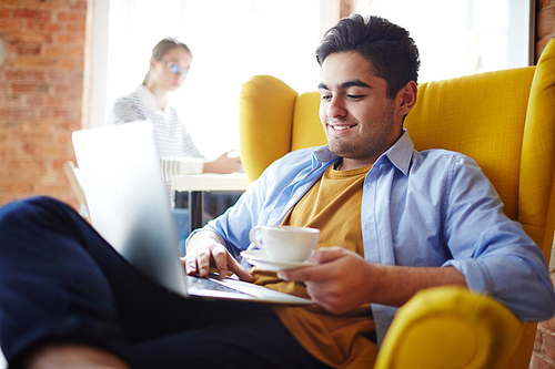 Relaxed man in comfortable armchair watching online video in laptop