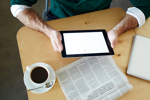 Human hands holding touchpad with financial data over table with newspaper and cup of coffee