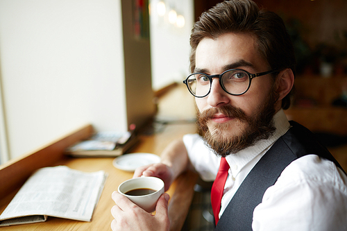 Young specialist or entrepreneur with cup of coffee having break in cafe