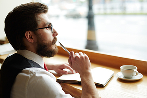 Posh young man with pen thinking of ideas while making notes in notebook