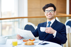 Cheerful businessman with drink and newspaper sitting in cafe