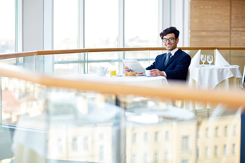 Successful young businessman with newspaper having breakfast in cafe