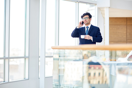 Elegant businessman with cup of tea speaking on cellphone