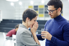 Hopeless woman with handkerchief crying in front of helpful man with glass of water