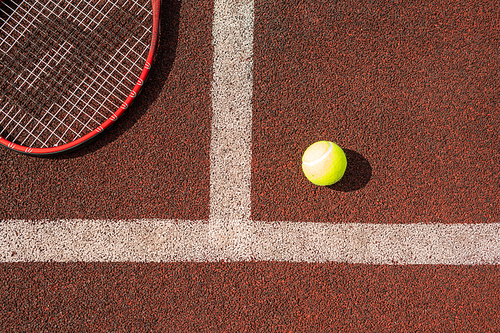 Overview of tennis ball and part of racket on playground by white line