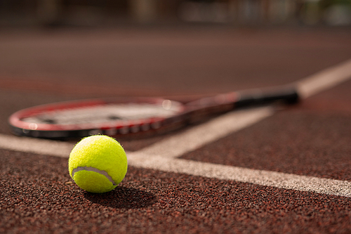 Yellow tennis ball on sports playground and tennis racket on background