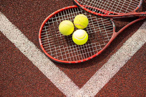 Top view of two tennis rackets and three yellow balls lying by crossing of white lines