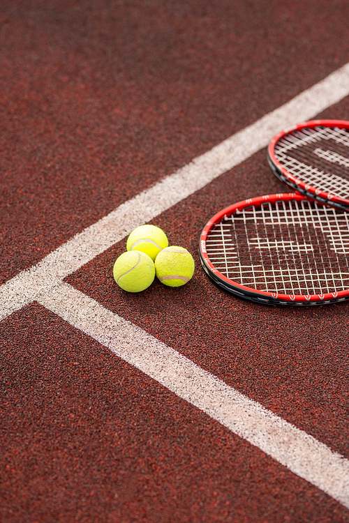 Two tennis rackets lying by white line close to three yellow balls