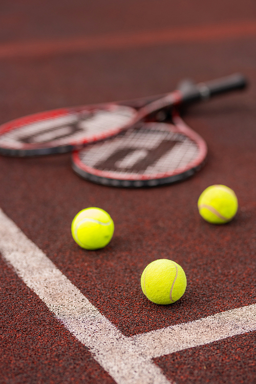 Three tennis balls by crossed white lines on court with two rackets on background