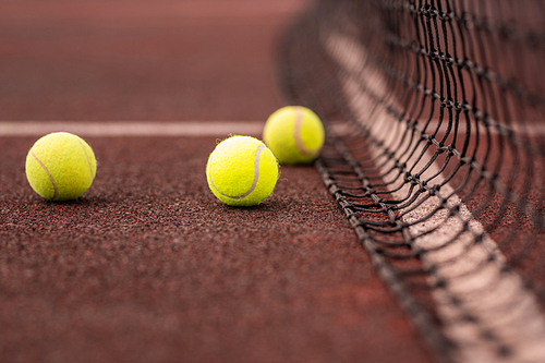Three yellow tennis balls on court or playground and net prepared for game
