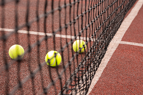 Three balls for playing tennis on playground behind black net with nobody around