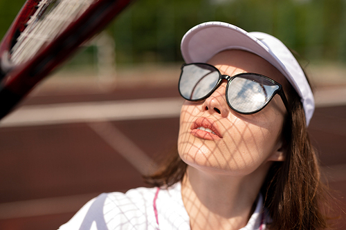 Young tennis player in sunglasses looking upwards while catching ball on sunny day