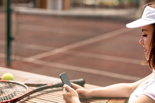 Young female tennis player messaging in her smartphone after game on stadium