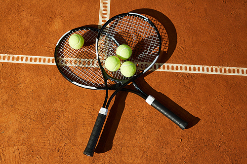 Overview of two tennis rackets with group of balls on top lying on court at stadium