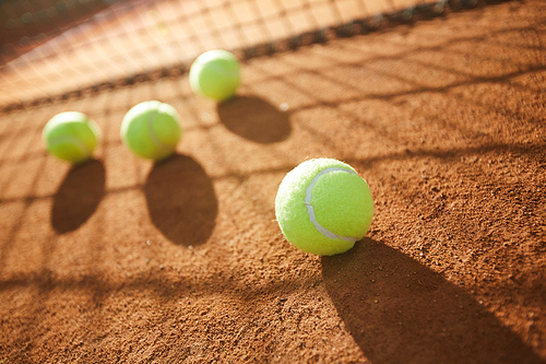 Group of tennis balls on sandy court of modern stadium with net on background