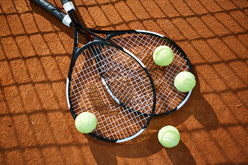 View of two new tennis rackets and several balls on court that can be used as background
