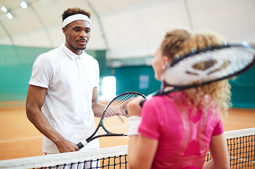 Young African-american tennis player talking to his playmate behind net on the court