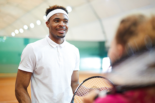 Happy young tennis player in activewear and headband chatting to his playmate at break