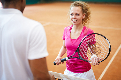 Young tennis player with racket standing on court in front of her playmate and discussing some details of game