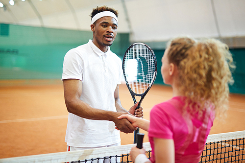 Young African-american man in activewear shaking hand of his playmate over net on the court