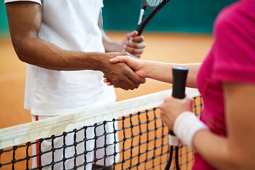 Handshake of intercultural tennis players over net after or before game on the court