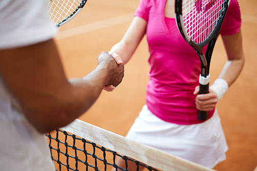 Young sportswoman with tennis racket shaking hand of her playmate over net