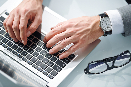 Top view of elegant contemporary businessman hands on keys of laptop keypad during network