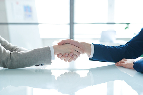 Handshake of two young contemporary colleagues or business partners over desk after negotiation and signing contract