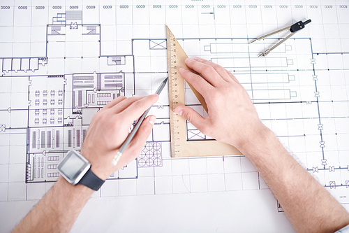Engineer with pencil drawing straight line by edge of wooden triangle measuring tool while working over sketch of construction