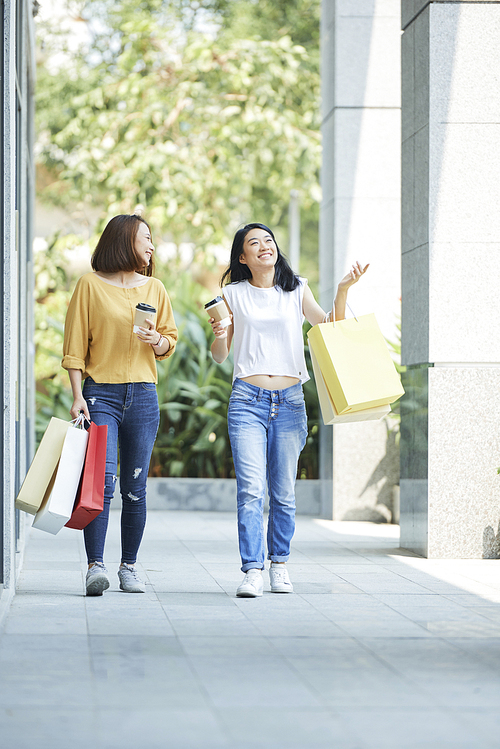 Happy pretty young women walking outdoors and talking after shopping at mall