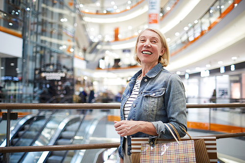 Cheerful excited mature woman with blond hair standing in shopping mall and laughing while 