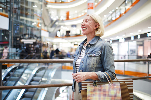 Positive attractive blond-haired mature woman in casual outfit going round shops in mall and enjoying weekend leisure