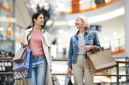 Cheerful confident women in casual clothing moving over corridor of shopping mall and sharing expressions from purchasing