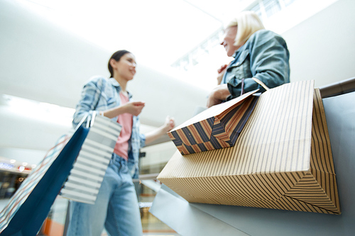 Focus on colorful paper shopping bags in hands of customers standing in shop and chatting together