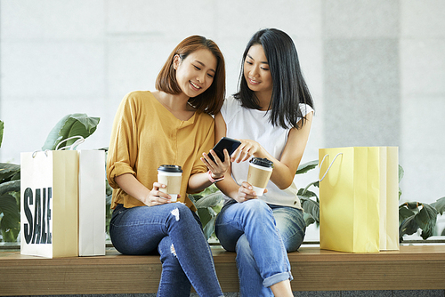 Pretty young Asian women drinking coffee and checking social media on smartphone
