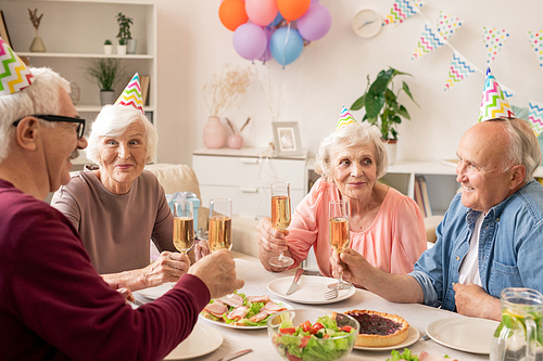 Group of senior people sitting by served table at home while celebrating birthday