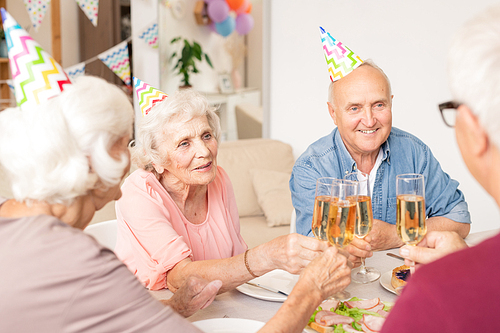 Group of happy senior friends clinking with flutes of champagne by served table