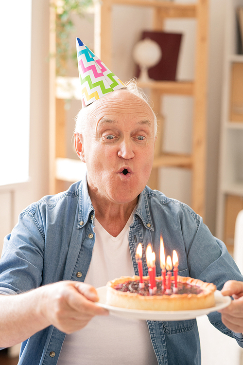 Aged man blowing candles on homemade birthday cake while celebrating alone