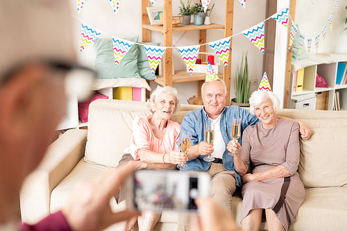 Three senior friends with flutes of champagne sitting on couch while toasting for birthday