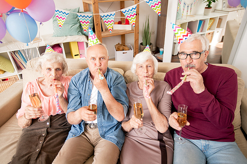Group of senior friends or two couples with champagne blowing whistles at birthday party