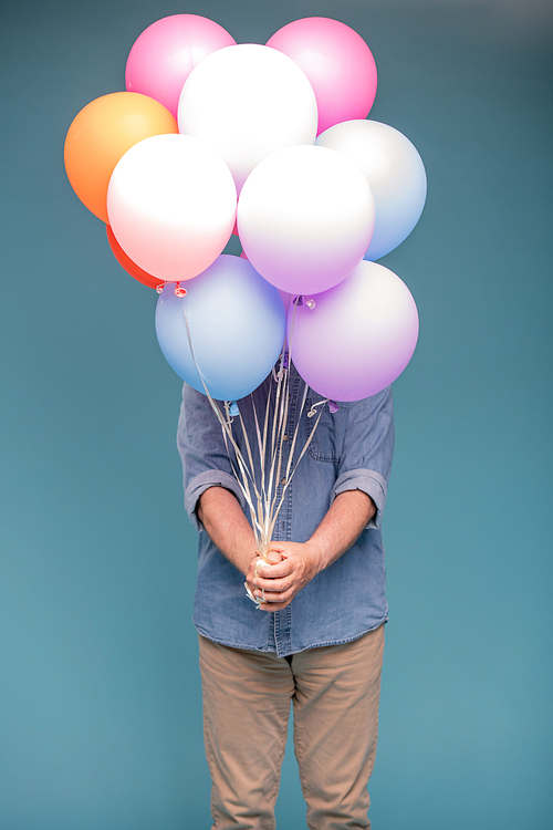 Mature man in casualwear holding bunch of colorful balloons while standing in isolation