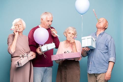 Two senior couples with giftboxes blowing whistles while having birthday fun