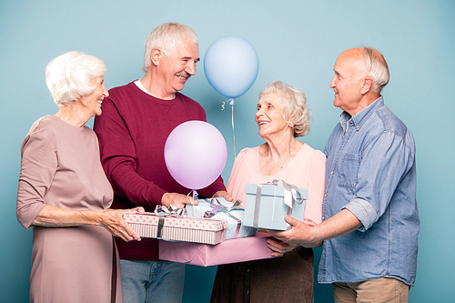 Cheerful company of friendly pensioners with balloons and giftboxes celebrating holiday or anniversary