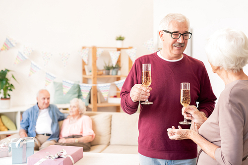 Senior spouses toasting with flutes of champagne while celebrating holiday with friends