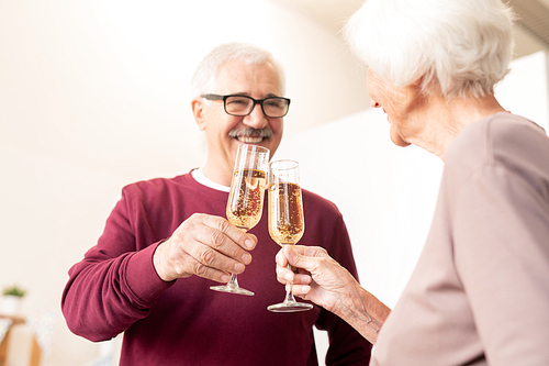 Mature husband and wife clinking with flutes of champagne at home party